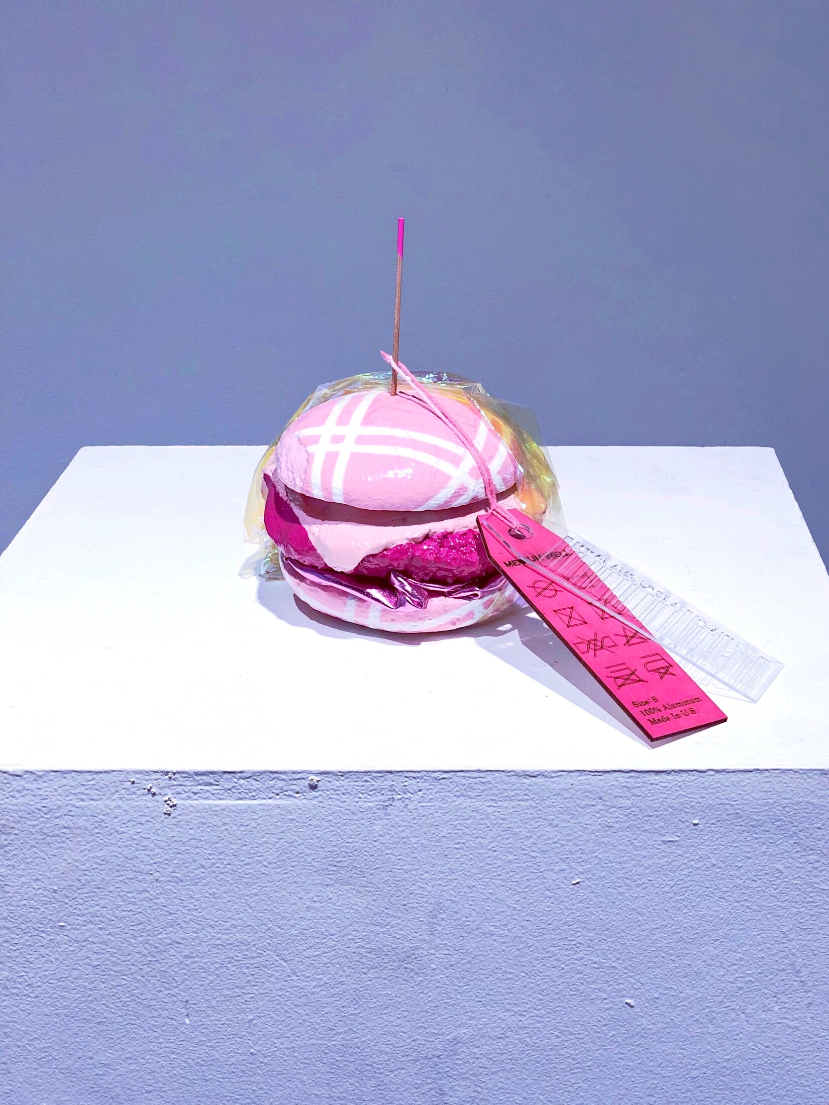 Medium Well, a cast aluminum hamburger sculpture painted in shades of pink with a garment-style tag